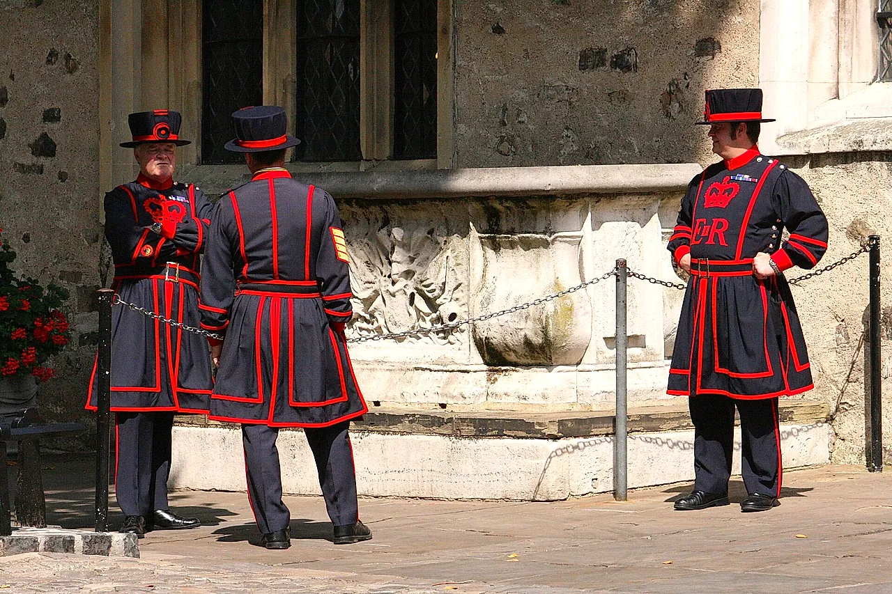 Three Yeoman Warders in their dark blue and red state dress standing in a sunlit courtyard of the Tower of London
