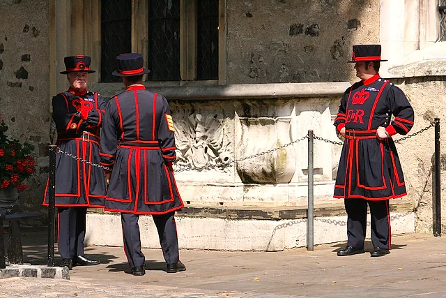 Three Yeoman Warders in their dark blue and red state dress standing in a sunlit courtyard of the Tower of London